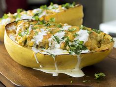 two yellow squash filled with food sitting on top of a wooden cutting board and covered in white sauce