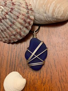 a blue sea glass pendant sitting on top of a wooden table next to a seashell