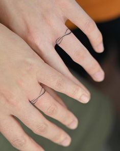 two people with wedding rings on their fingers, one has a small wave tattoo on it's ring finger