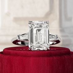 an emerald - cut diamond ring sits atop a red velvet stand