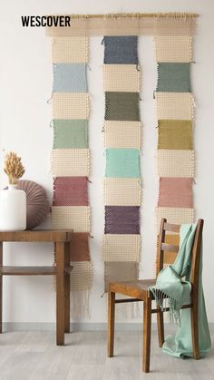 two chairs and a table in front of a wall hanging with different colored yarns