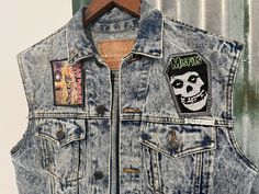 Let your rebellious side out in this vintage 1990's denim vest. A classic trucker vest in awesome stonewash denim. It features a turn down collar, metal buttons, two front patch pockets with flaps and two hand-warmer pockets.  It has been hand decorated with Iron Maiden and Misfits patches on the front plus a large Jack Daniels patch on the back. It also has a silver skull stud on the collar.  One of a kind Size Small. Measurements:                                                                                                                    Chest: 92 cms / 36 inches                                                                                                Length: 61 cms / 24 inches        BUYING VINTAGE: While all care is taken to state any obvious faults, please note that when yo Distressed Punk Denim Vest For Streetwear, Fitted Punk Cotton Denim Jacket, Punk Distressed Denim Vest For Streetwear, Fitted Punk Style Cotton Denim Jacket, Fitted Cotton Punk Denim Jacket, Cotton Grunge Denim Vest For Streetwear, Distressed Denim Vest For Streetwear In Grunge Style, Distressed Grunge Denim Vest For Streetwear, Vintage Cotton Denim Jacket For Festival