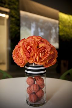 a vase filled with orange flowers sitting on top of a white round table covered in balls