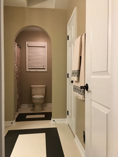 a white toilet sitting in a bathroom next to a doorway with a black and white floor