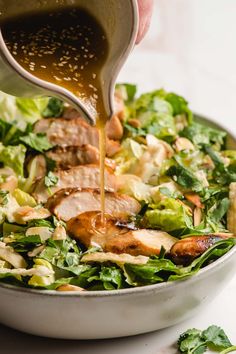 someone pouring dressing onto a salad with chicken and lettuce in a white bowl