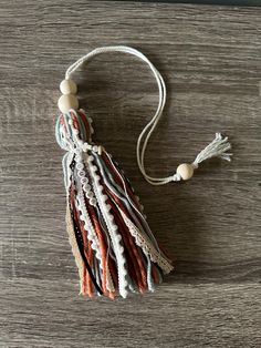 the tasseled necklace is made from fabric and beads on a wooden surface with a white cord