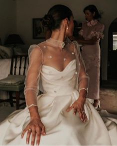 a woman in a white wedding dress sitting on a bed with another woman standing behind her