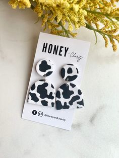 the black and white cow print earrings are on top of a card next to some flowers