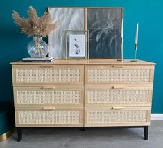 a wooden dresser with two pictures on top and a vase filled with dried flowers next to it