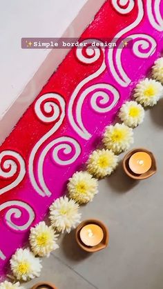 some candles and flowers are sitting on the floor next to a red wall with white swirls