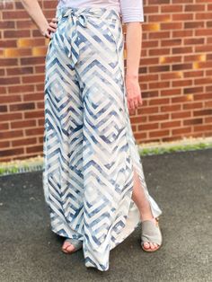 a woman standing in front of a brick wall wearing a white shirt and blue patterned skirt