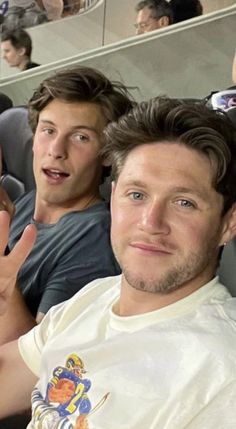 two young men sitting next to each other in front of an audience with their thumbs up