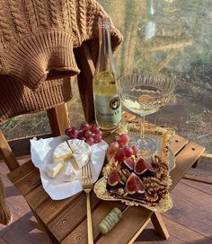 a wooden table topped with food and wine next to a glass filled with wine on top of a wooden deck