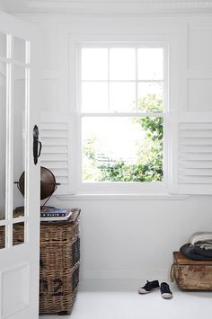 an open window in a white room with shoes on the floor and luggage under it