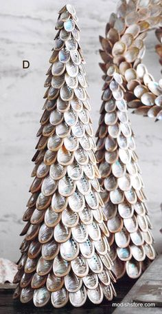 two metal christmas trees sitting next to each other on a wooden table with seashells in them