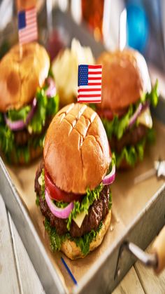 two hamburgers with american flags on them sitting on a tray next to potato wedges