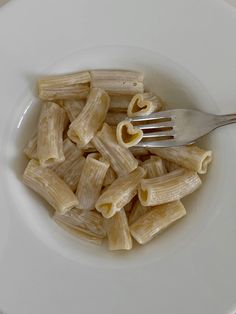 a white bowl filled with pasta on top of a table next to a silver fork