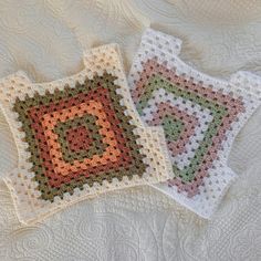 two crocheted squares sitting on top of a white bed spread with the same pattern