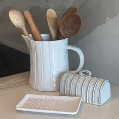 a white mug filled with wooden spoons on top of a counter next to a coaster