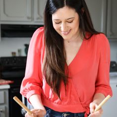 a woman in a red shirt is holding two wooden sticks and looking at something on the counter