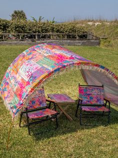 two lawn chairs sitting under an umbrella in the middle of a grassy field next to a picnic table