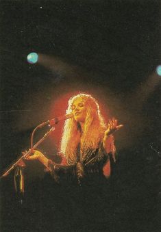 a woman standing in front of a microphone on top of a stage with lights behind her