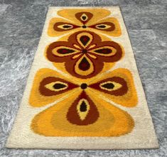 a yellow and brown rug on the floor with an orange flower design in the middle