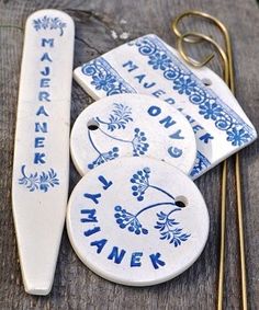 three blue and white ceramic tags with gold handles on wooden boards next to knitting needles