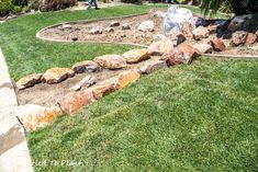 there is a rock garden in the middle of the grass and people are walking around