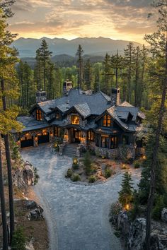 an aerial view of a home surrounded by trees and mountains at dusk with lights on the windows