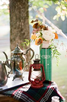 a table topped with a vase filled with flowers and a lantern next to a tea kettle