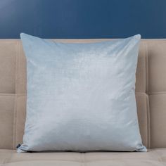 a light blue pillow sitting on top of a beige couch next to a blue wall