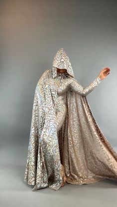 a woman in a silver dress with a hood on her head and hands behind her back