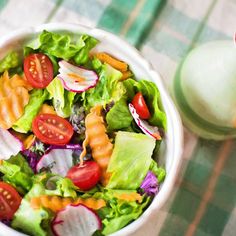 a salad with tomatoes, lettuce and onions in a white bowl next to a green teapot