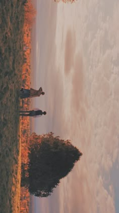 two people are standing in the grass looking out at the sky and clouds behind them