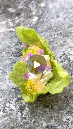 an object made out of green leaves and flowers on top of a stone surface with a video player in the center