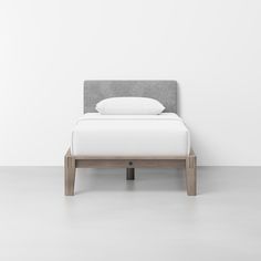 a bed with a gray headboard and white sheets on it, against a white wall