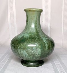 a large green vase sitting on top of a white tablecloth covered floor next to a curtain