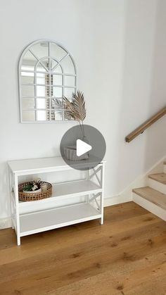 a living room with white walls and wooden floors, a mirror on the wall, and a plant in a basket