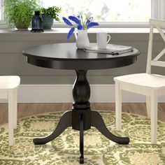 a black table with two white chairs and a potted plant on the window sill