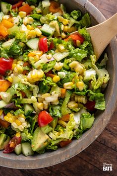 a salad with corn, tomatoes and lettuce in a bowl on a wooden table