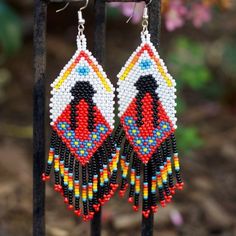 a pair of beaded earrings hanging from a metal rack with flowers in the background