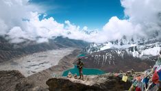 a man standing on top of a mountain next to a body of water and clouds