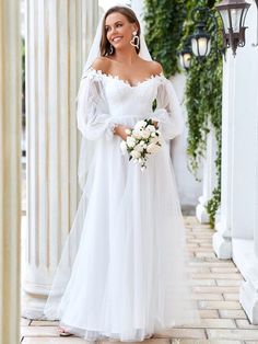 a woman in a white wedding gown standing on a brick walkway with columns and greenery behind her