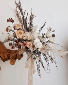 a woman holding a bouquet of flowers in front of a white wall with dried plants