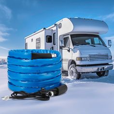 an rv is parked in the snow next to a blue hose and a white truck