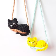 two crocheted cats hanging from strings on a white wall, one is black and the other is yellow