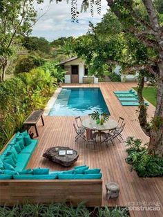 an outdoor living area with blue couches and tables next to a pool surrounded by trees