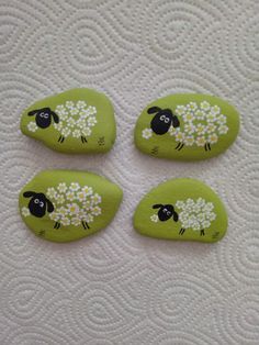 three green rocks with sheep painted on them and daisies in the middle, sitting on a white surface