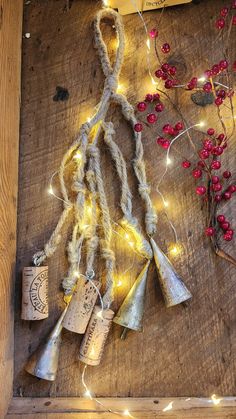 christmas lights and bells are hanging on a wooden board with twine rope, red berries, and tinsel